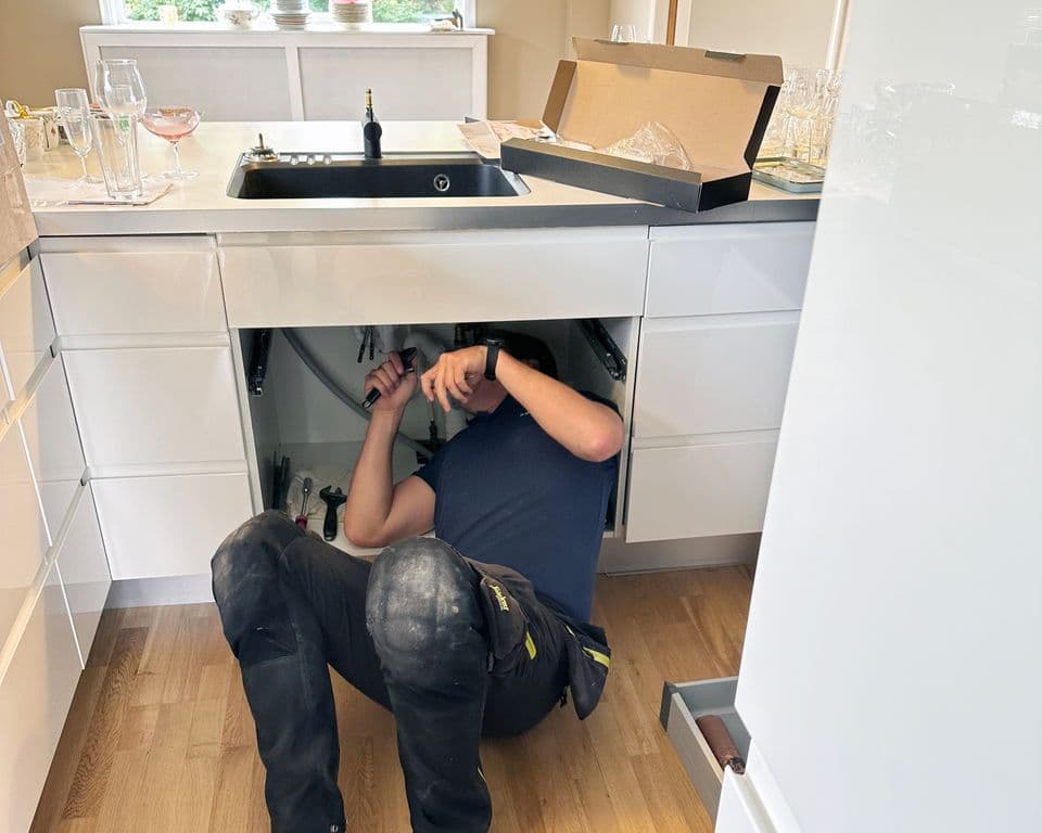 Rørlegger i arbeid under kjøkkenkum